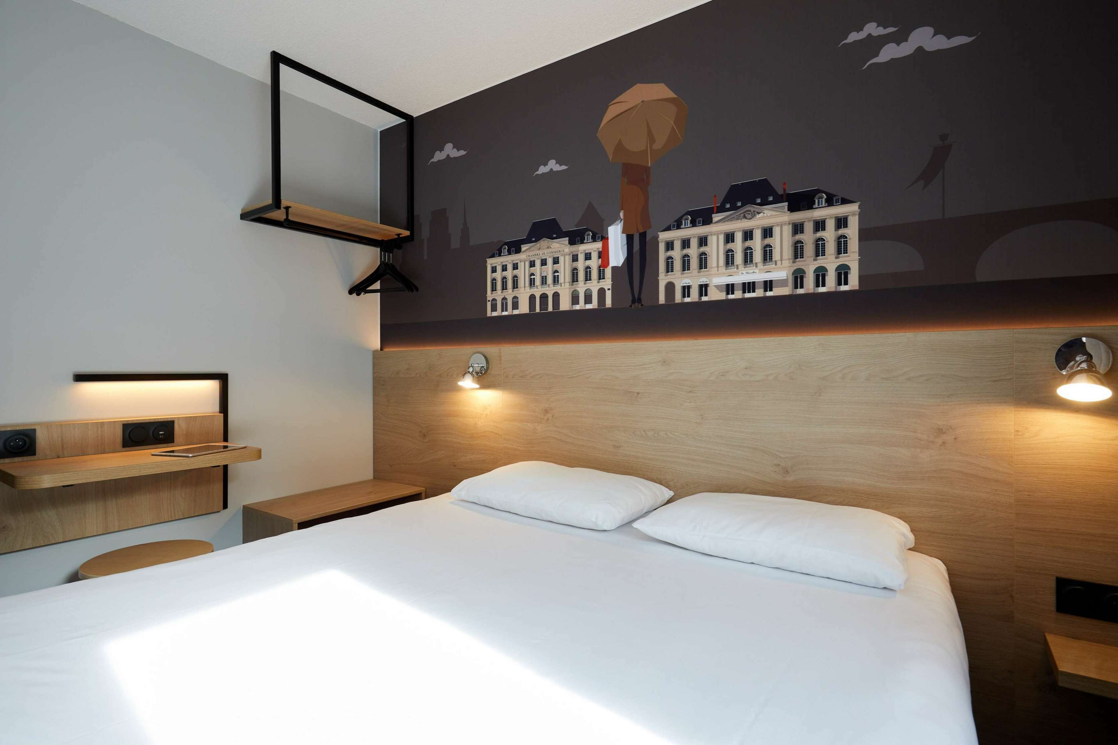 Una habitación de hotel moderna con una cama grande, cabecero de madera y un mural con vistas a la ciudad.