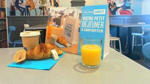 Desayuno con un croissant, jugo y una taza de café sobre una mesa, con un cartel de fondo.
