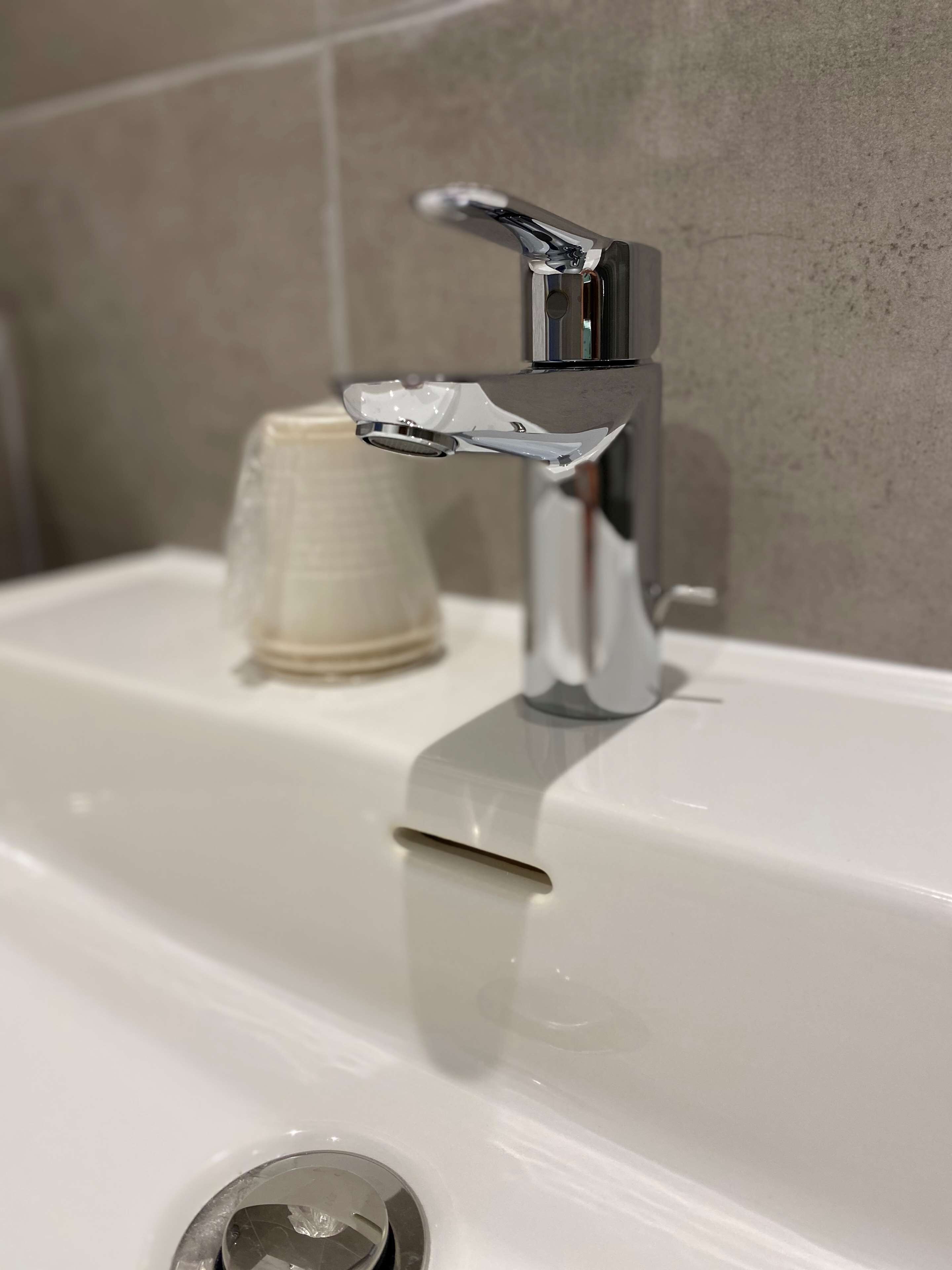 A modern bathroom with a chrome faucet, a white sink, and a cup holder.