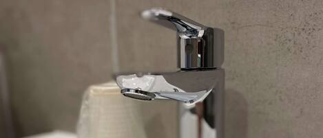 Un baño moderno con grifo cromado, un lavamanos blanco y un portavasos.