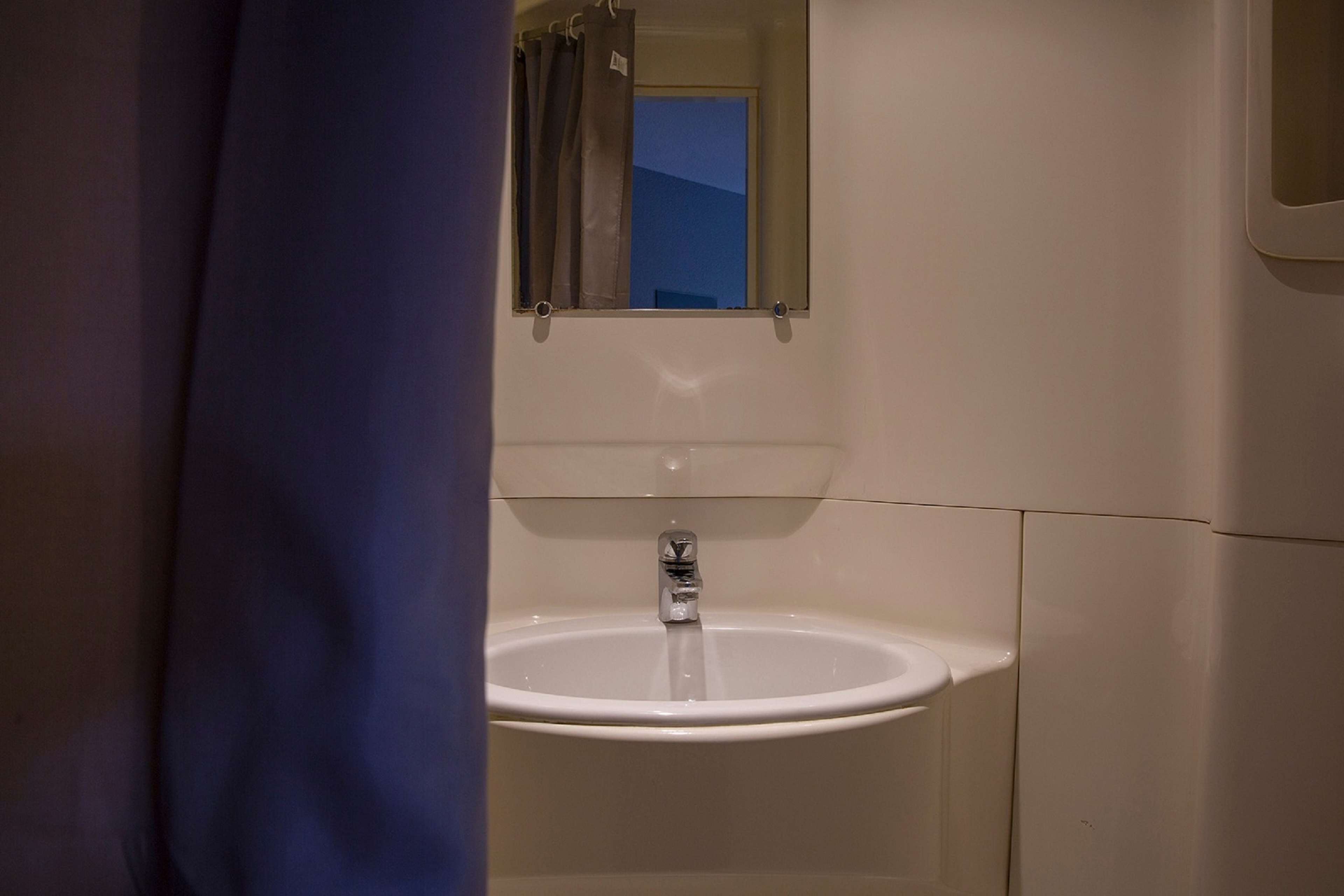Un baño con un lavamanos blanco, un espejo encima y una ventana con cortinas.