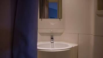 Un baño con un lavamanos blanco, un espejo encima y una ventana con cortinas.