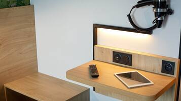 Een houten nachtkastje met een afstandsbediening, een tablet en een wandlamp.