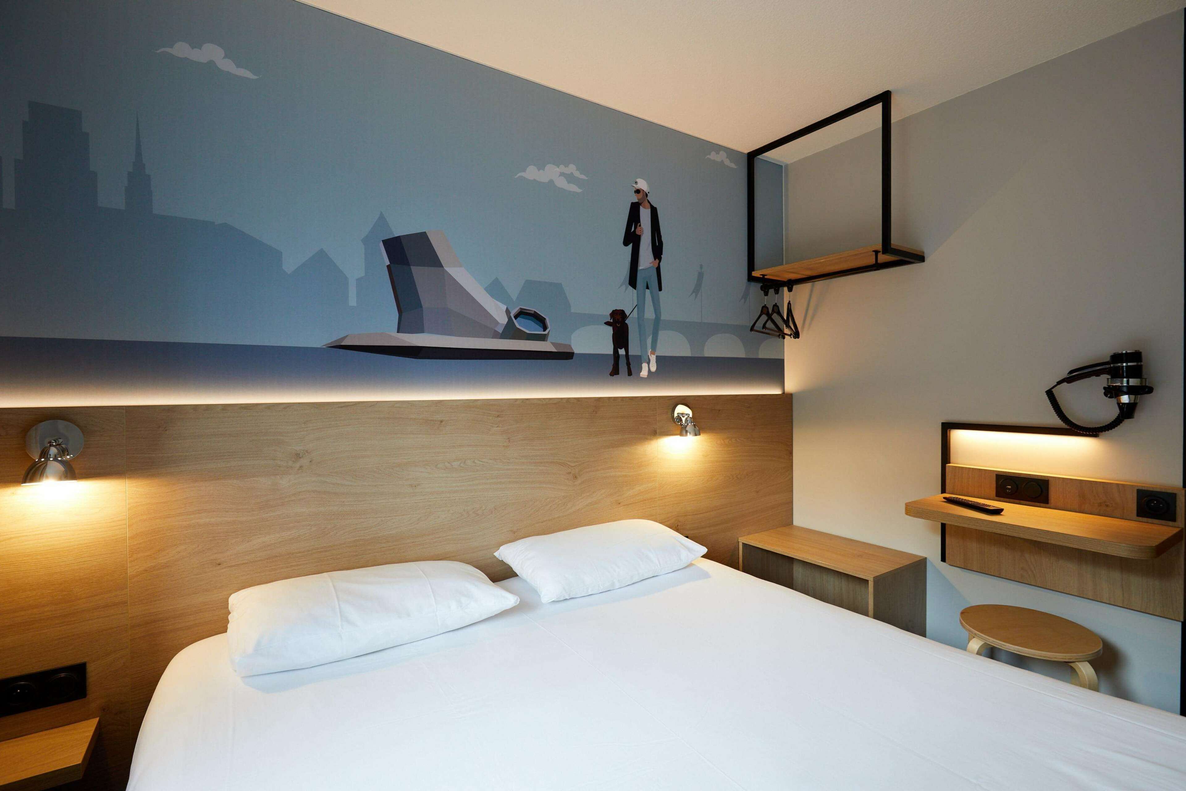 Quarto de hotel moderno com uma cama grande, cabeceira de madeira, televisão fixada na parede e uma mesinha.