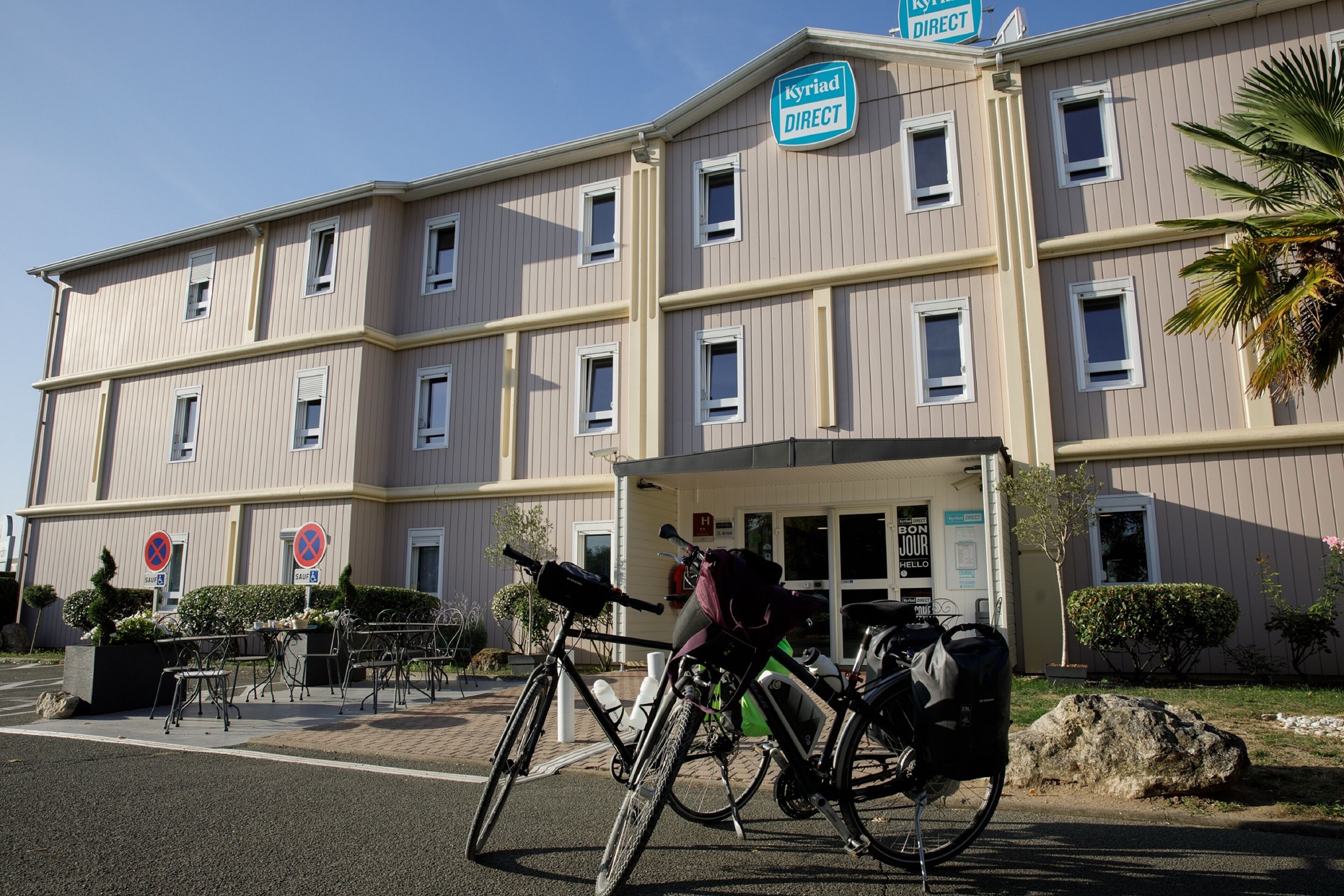 Een meerhoog hotel met een bord waarop 'Kyriad Direct' staat en een fiets ervoor geparkeerd.