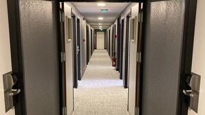 Un pasillo de hotel con pisos alfombrados, puertas a ambos lados y un extintor de incendios a la derecha.