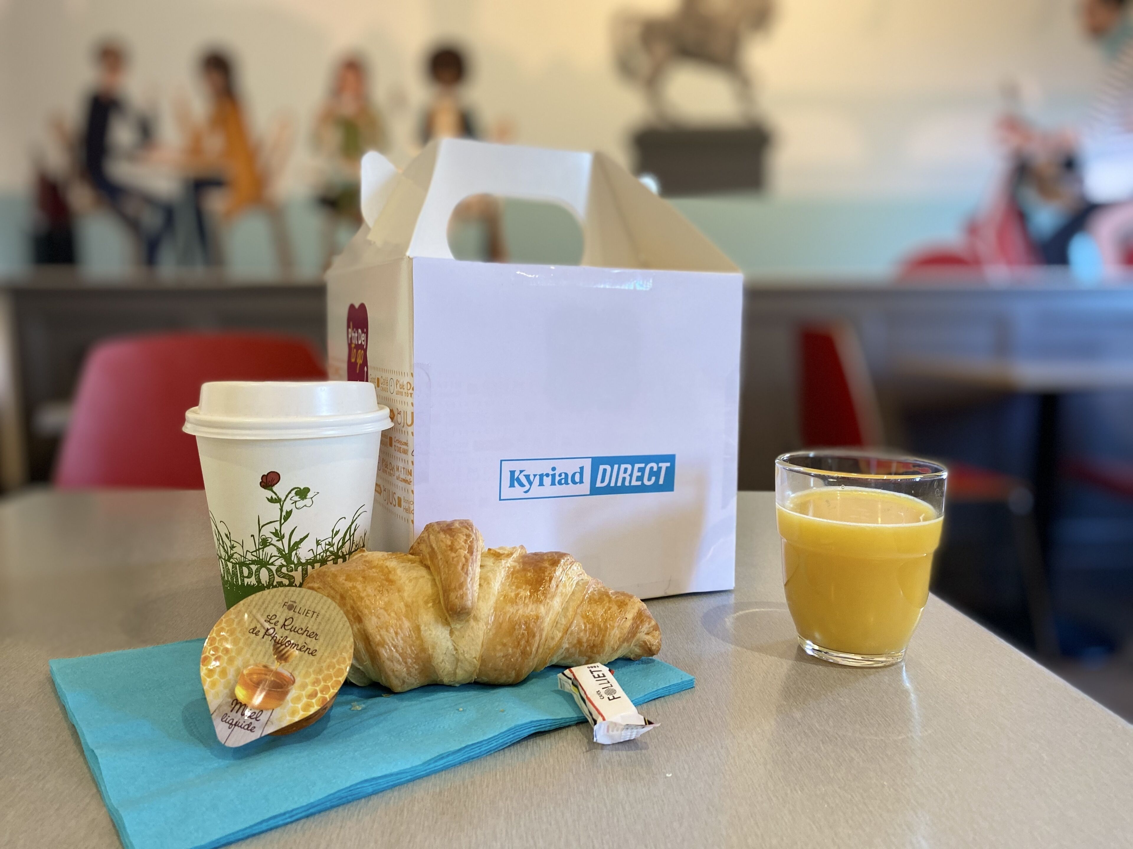 Pöydällä on croissant, kahvikuppi, mehulasi ja maitopullo.