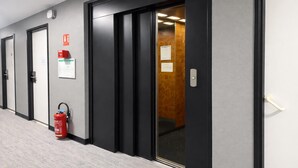 Un pasillo con puertas, un extintor y señales de salida de emergencia.