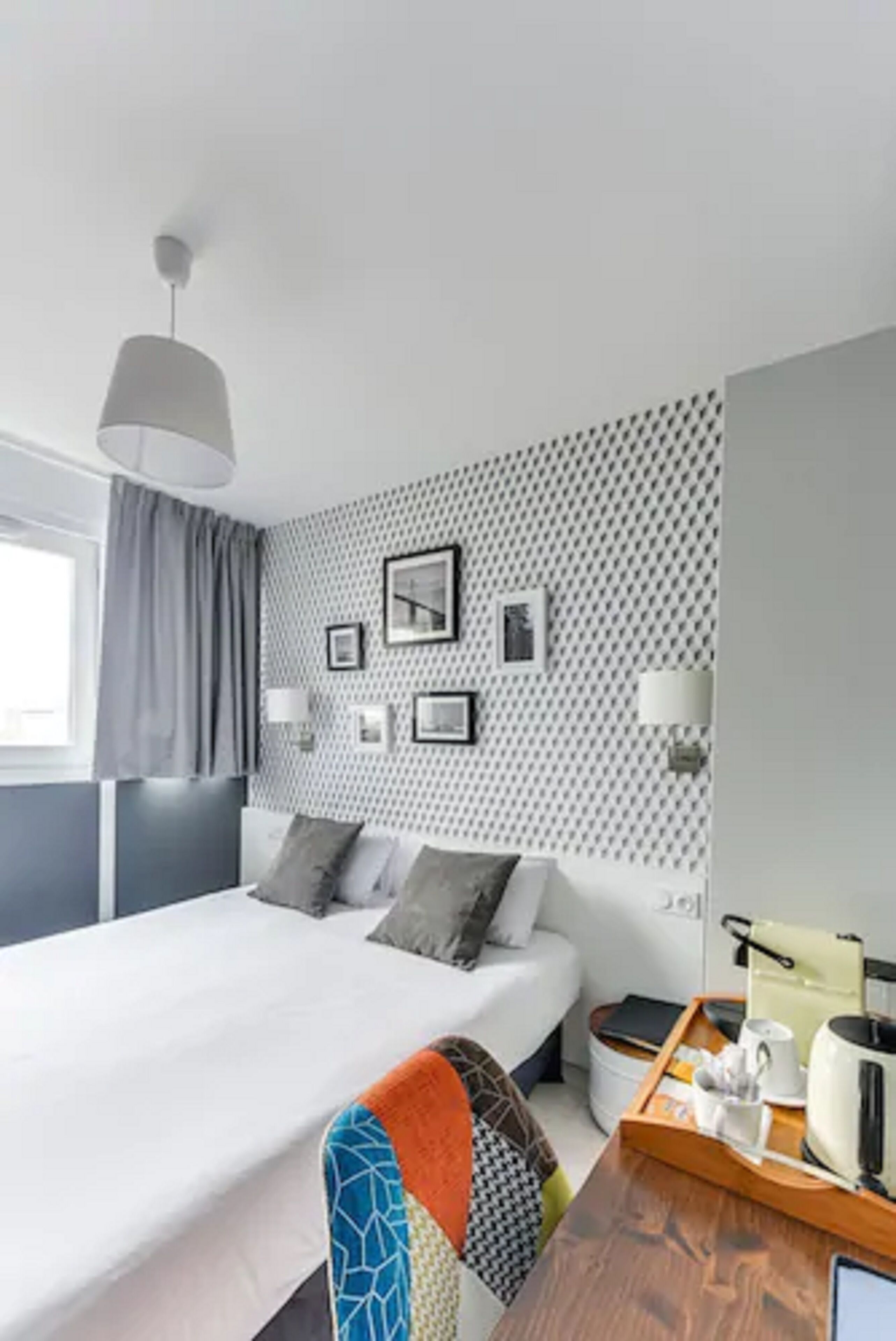 A modern hotel room with a large bed, a bedside table with a kettle, and a tray with a cup and a book.