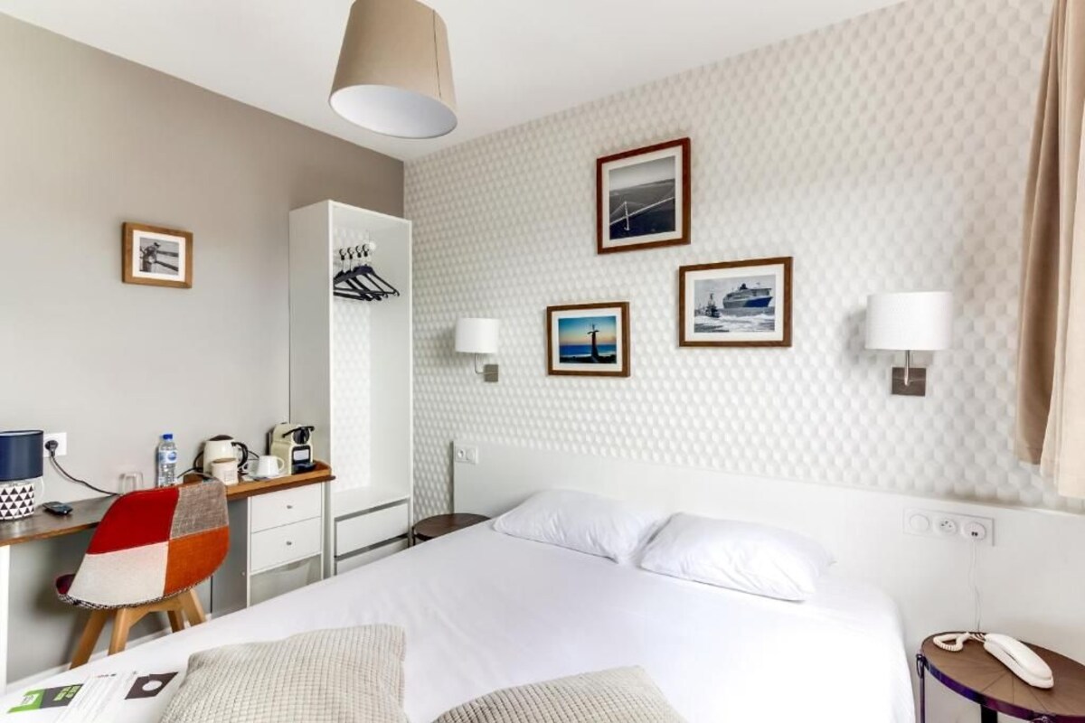 A hotel room with a bed, a desk with a chair, a wardrobe, and wall-mounted lamps.