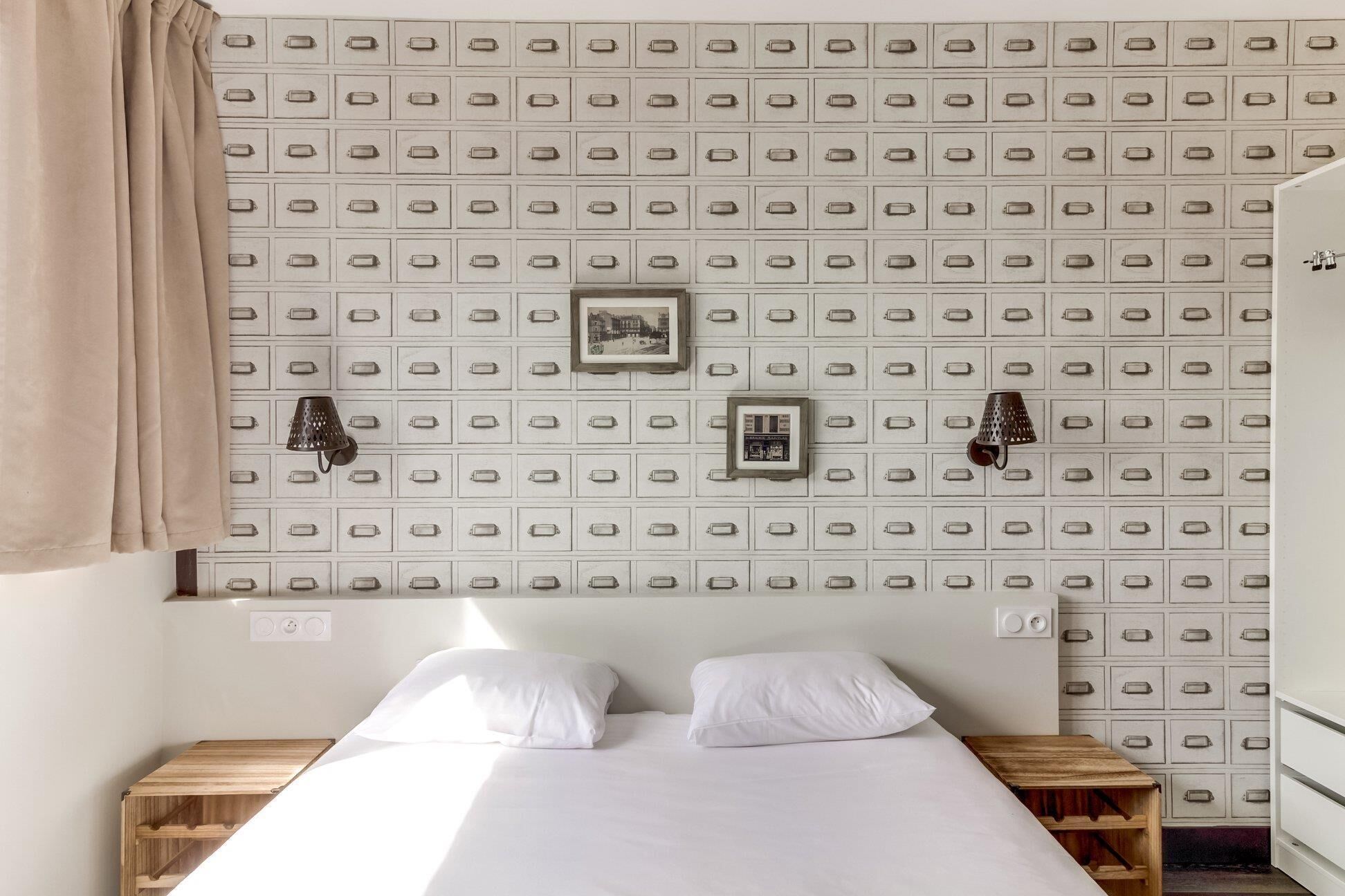 Un dormitorio con una cama, dos mesitas de noche, una lámpara de pared y un papel tapiz estampado.