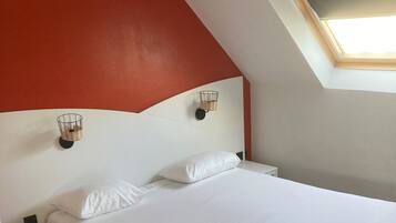 A bedroom with a white bed, a nightstand, a red accent wall, and a skylight.