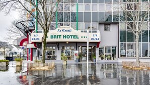 Een modern hotel met een glazen gevel, een bord met beschikbaarheid 24 uur per dag, 7 dagen per week, en een basketbalveld ervoor.