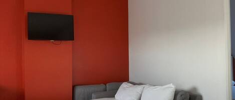 A modern room with a bed, a TV mounted on the wall, a dining table with chairs, and a small plant on the table.