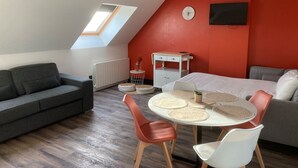 Een gezellige kamer met een schuine kap, een grijze bank, een wit bed, een klein tafeltje met stoelen en een rode accentmuur.
