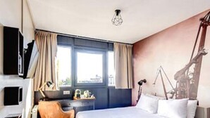 Een moderne hotelkamer met een groot bed, een bureau met stoel, een televisie en een raam met gordijnen.