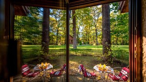 A dining area with a table set for four, surrounded by chairs, and a view of a wooded area with a small building in the distance. - Park Hotel Drevny Grad (Lviv)