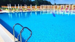 A swimming pool with a metal ladder, lounge chairs, and umbrellas. - Park Hotel Drevny Grad (Lviv)