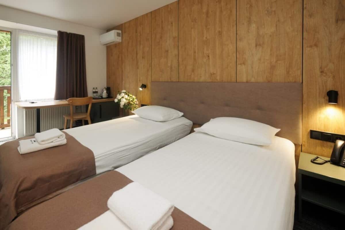 A hotel room with two beds, a desk, a chair, a telephone, and a window with curtains.