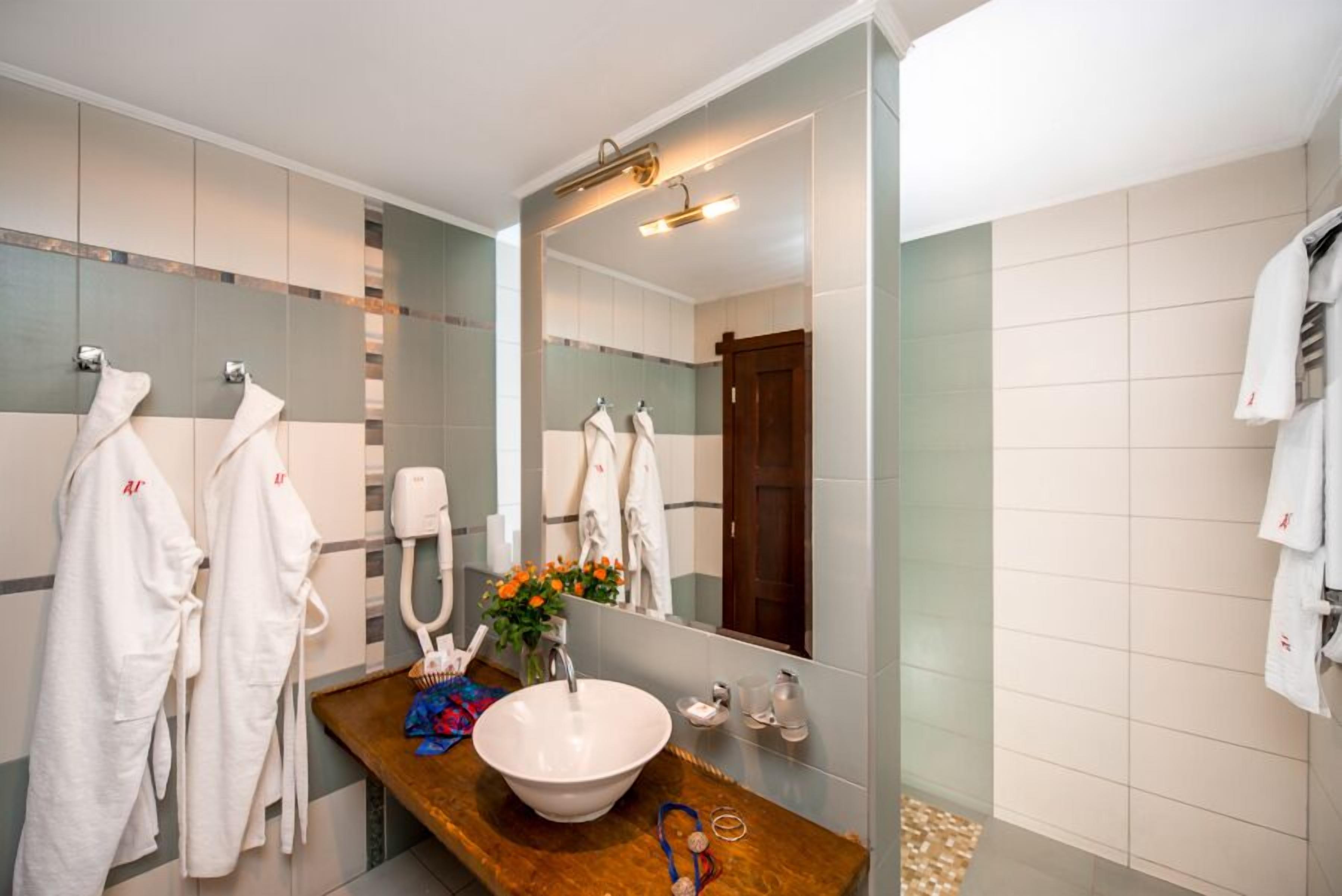 Une salle de bain moderne avec un grand miroir, un meuble-lavabo en bois, un lavabo blanc et plusieurs serviettes blanches suspendues à des crochets.