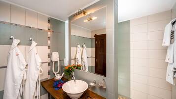 Une salle de bain moderne avec un grand miroir, un meuble-lavabo en bois, un lavabo blanc et plusieurs serviettes blanches suspendues à des crochets.