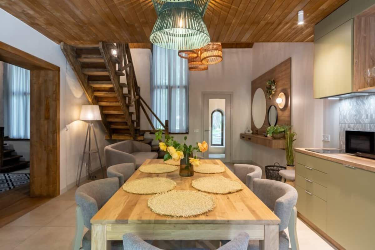 A modern kitchen with a wooden table, chairs, and a staircase.