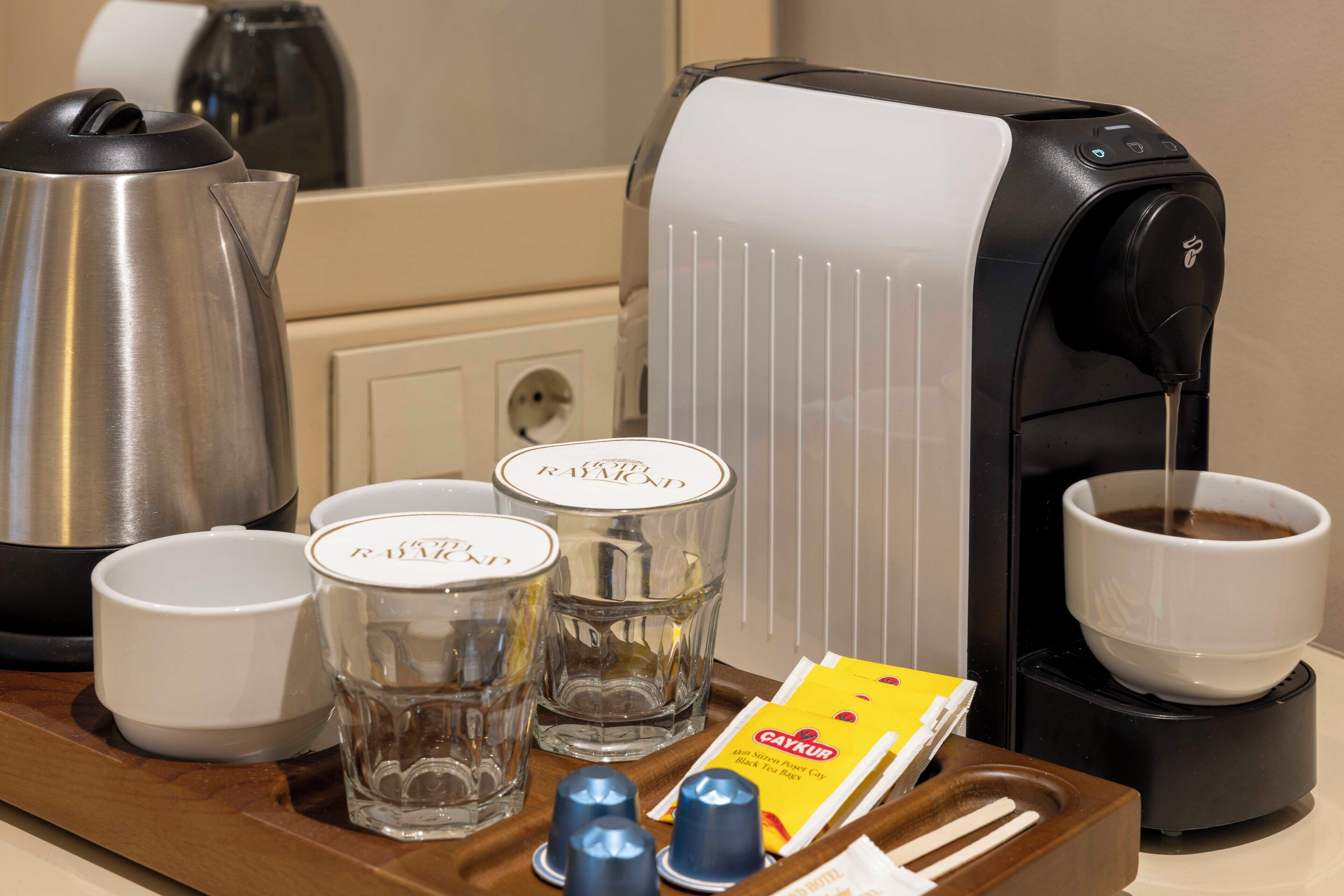 A coffee station with a coffee maker, cups, glasses, and a tray with coffee pods and a box.