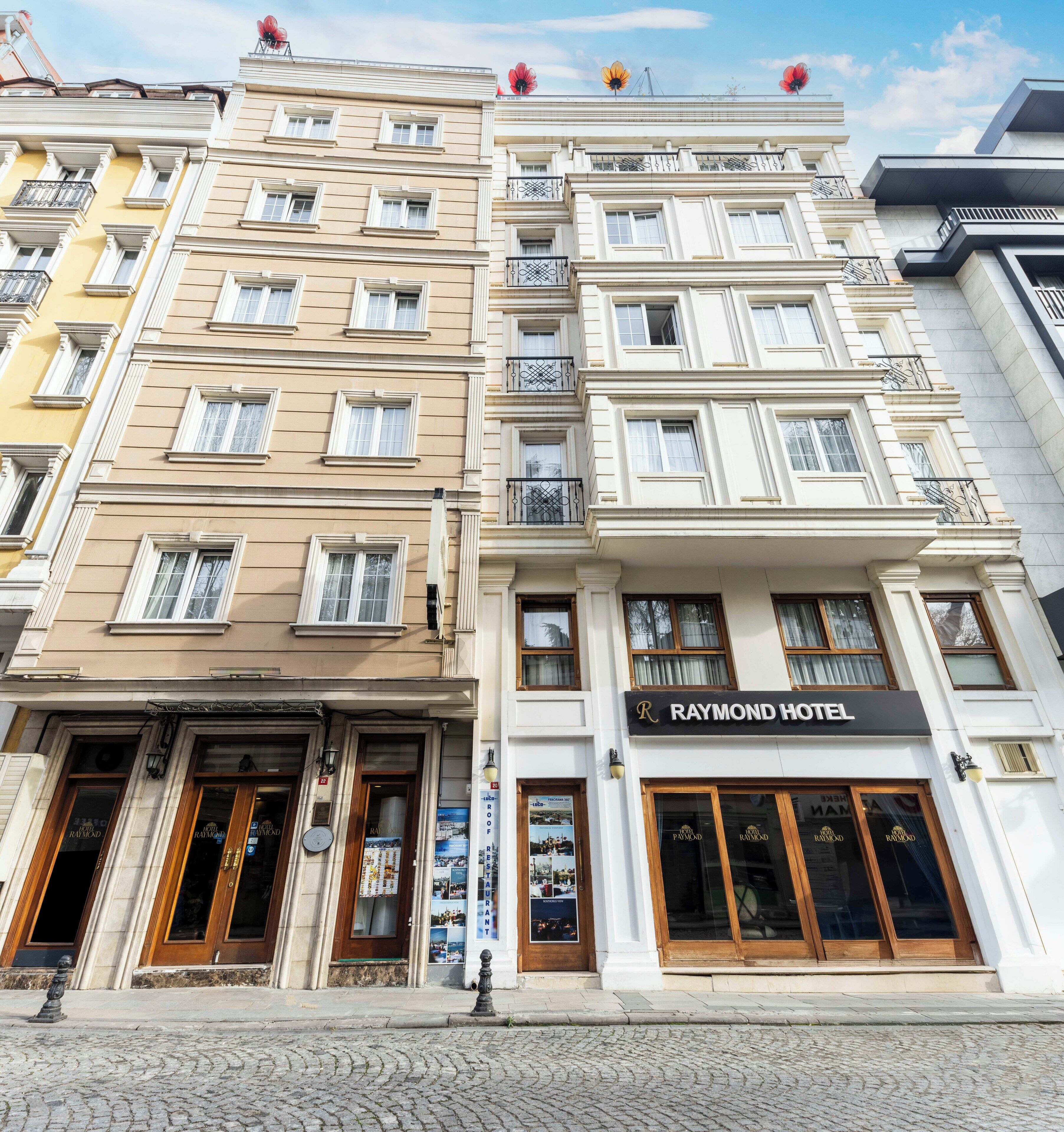 A multi-story hotel with a classic facade, featuring a prominent 'Raymond Hotel' sign.