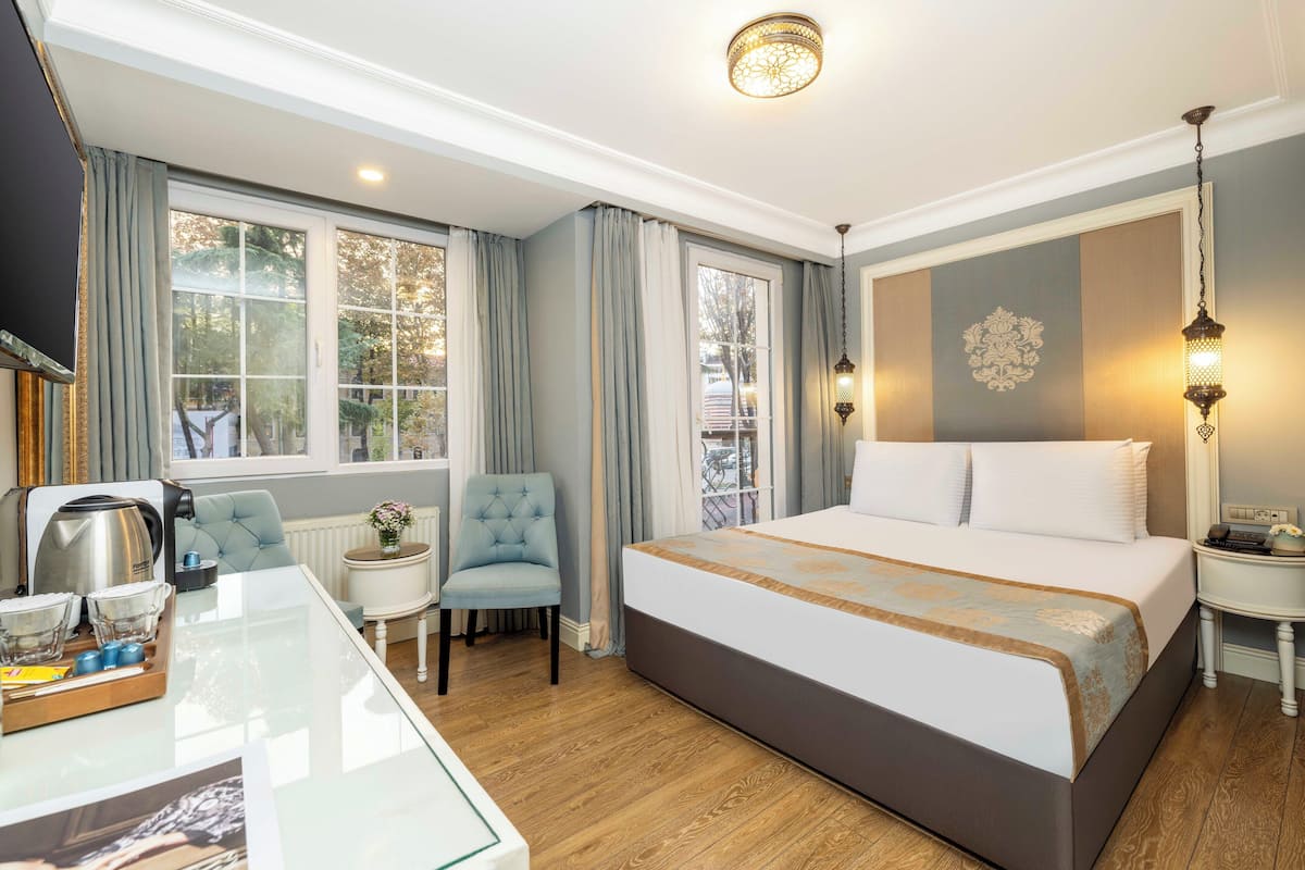 A hotel room with a large bed, a sitting area with a table and chair, a coffee maker, and a view of the outdoors through the windows.