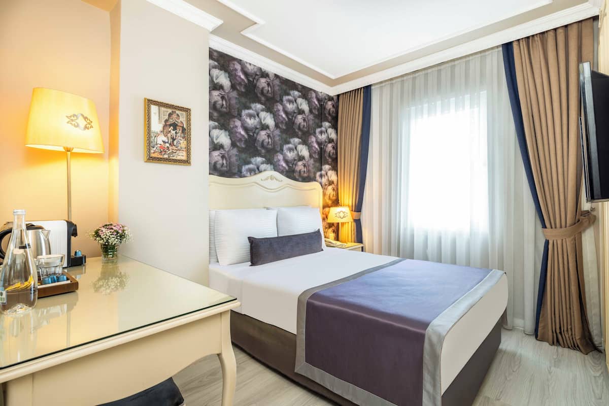 A hotel room with a bed, a desk, a lamp, a painting, and a TV.