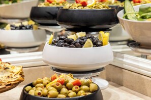 Een buffet met diverse gerechten, waaronder olijven, citroenen en een salade.