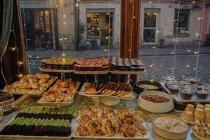 Diversos pastissos i postres exposats sobre una taula davant d'un edifici, amb un carrer empedrat i edificis al fons.