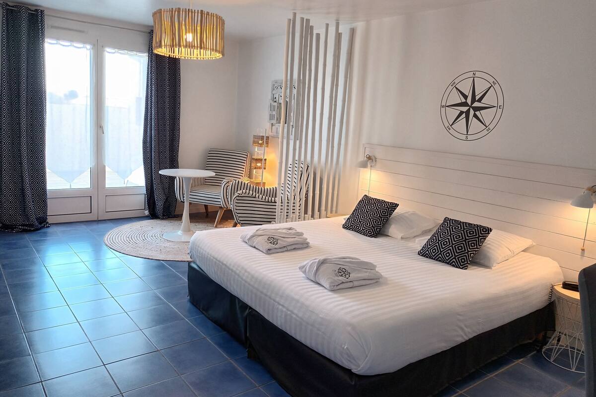 A modern hotel room with a large bed, a small table, a chair, and a decorative wall piece.