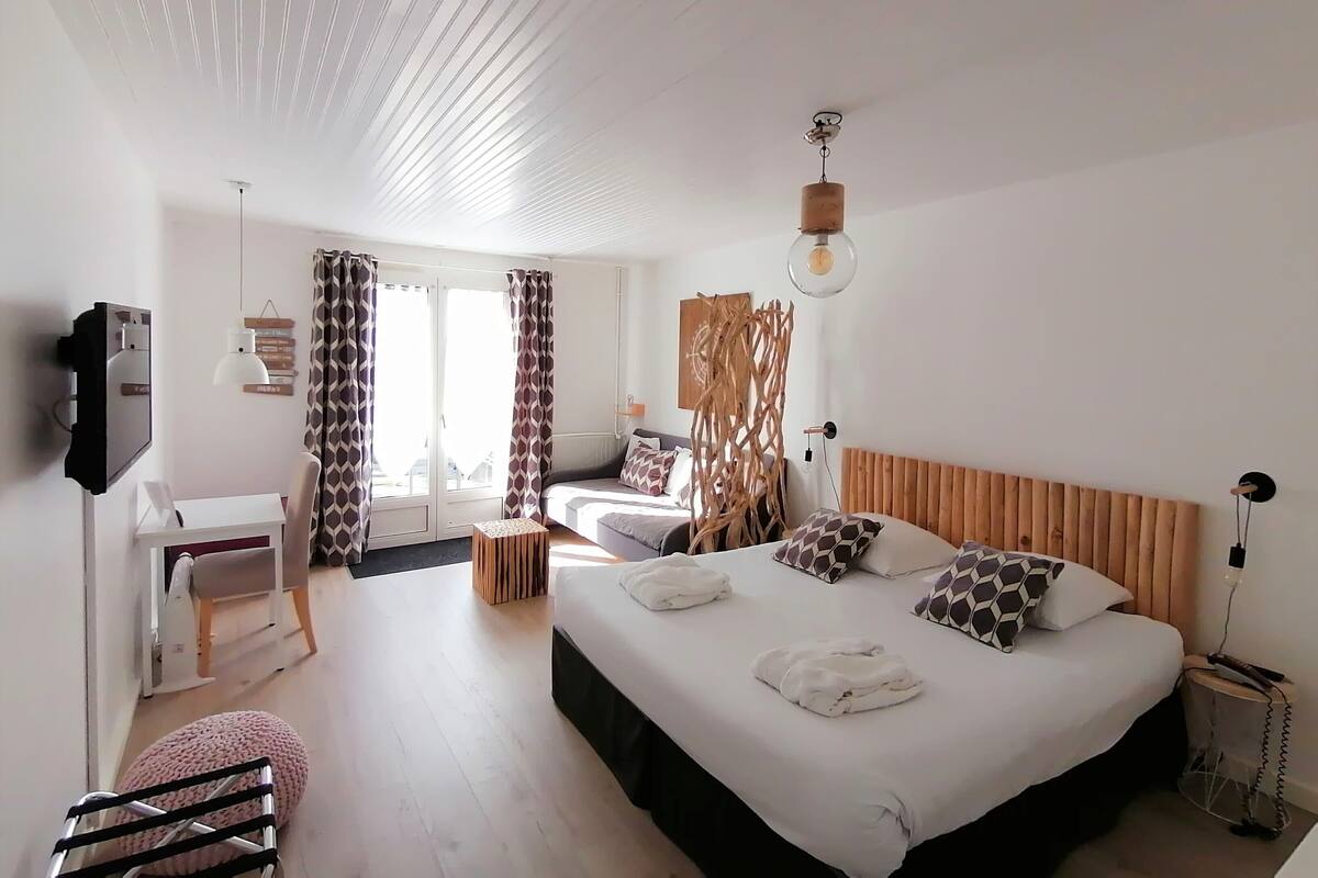 A hotel room with a bed, bedside table, chair, and a desk with a computer.