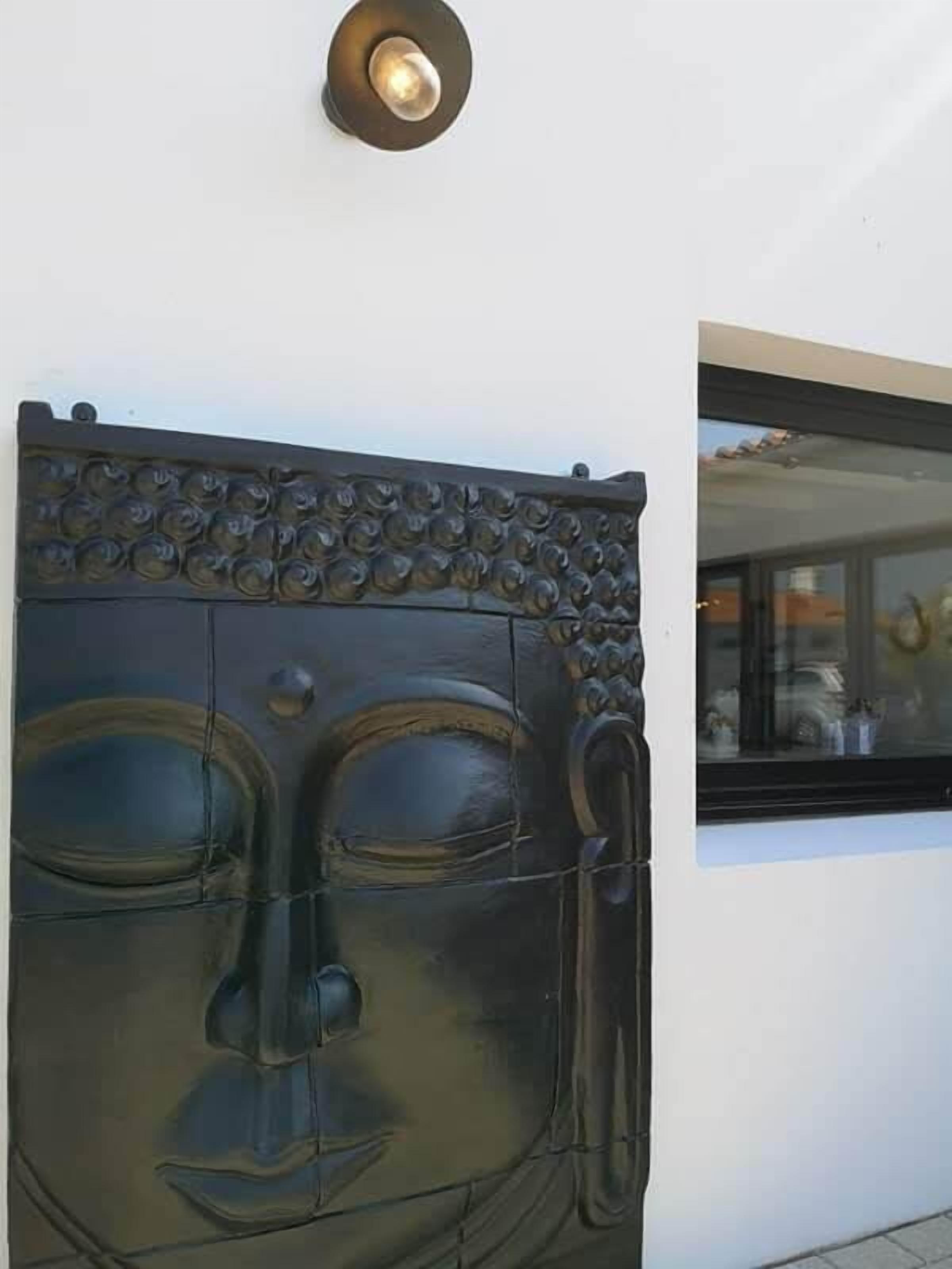 Suuri, tummanvärinen Buddha-patsas on kiinnitetty seinään, ja sen yläpuolella on pieni ikkuna.