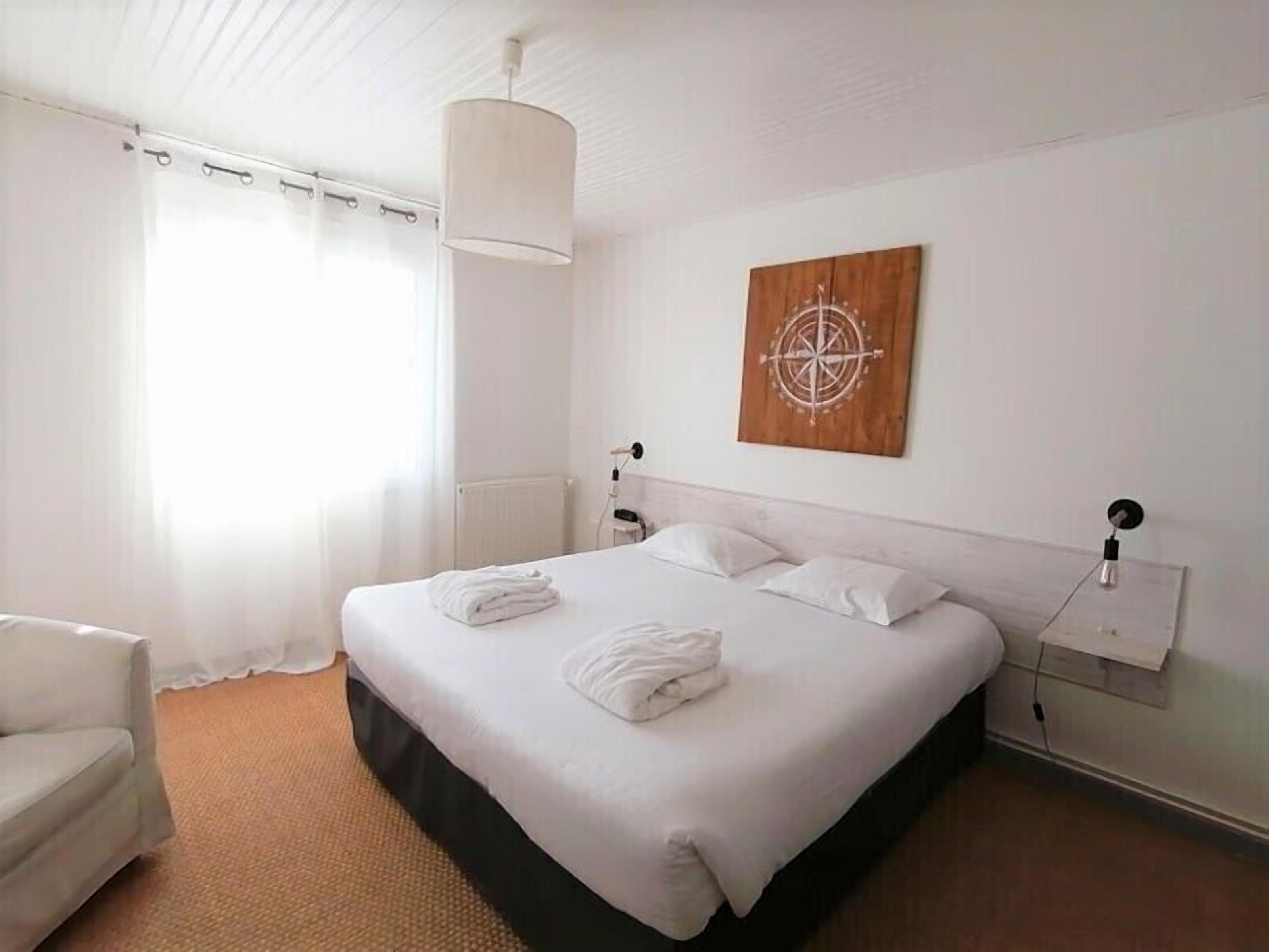 Una camera d'albergo con un letto grande, lenzuola bianche, un'opera d'arte a parete in legno e una sedia bianca.