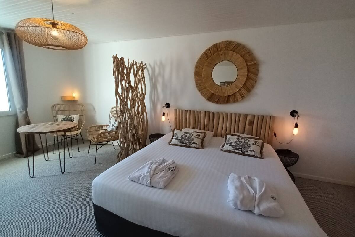 A hotel room with a large bed, two bedside tables, a chair, a hanging light fixture, and a wall-mounted mirror.