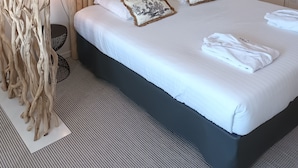 A neatly arranged bedroom with a large bed, a hanging light fixture, a round mirror, and a wooden headboard.