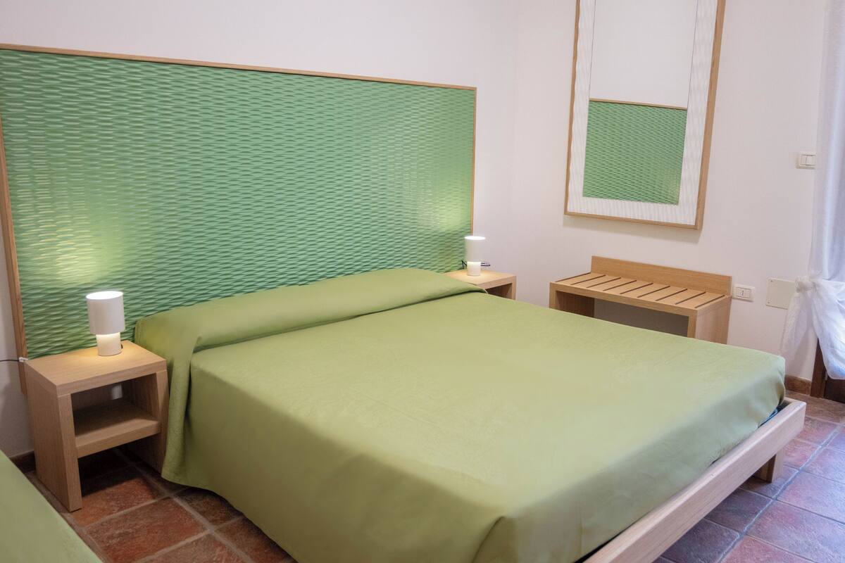 Una cama con un edredón verde, una mesita de noche con una lámpara y un cabecero de madera.