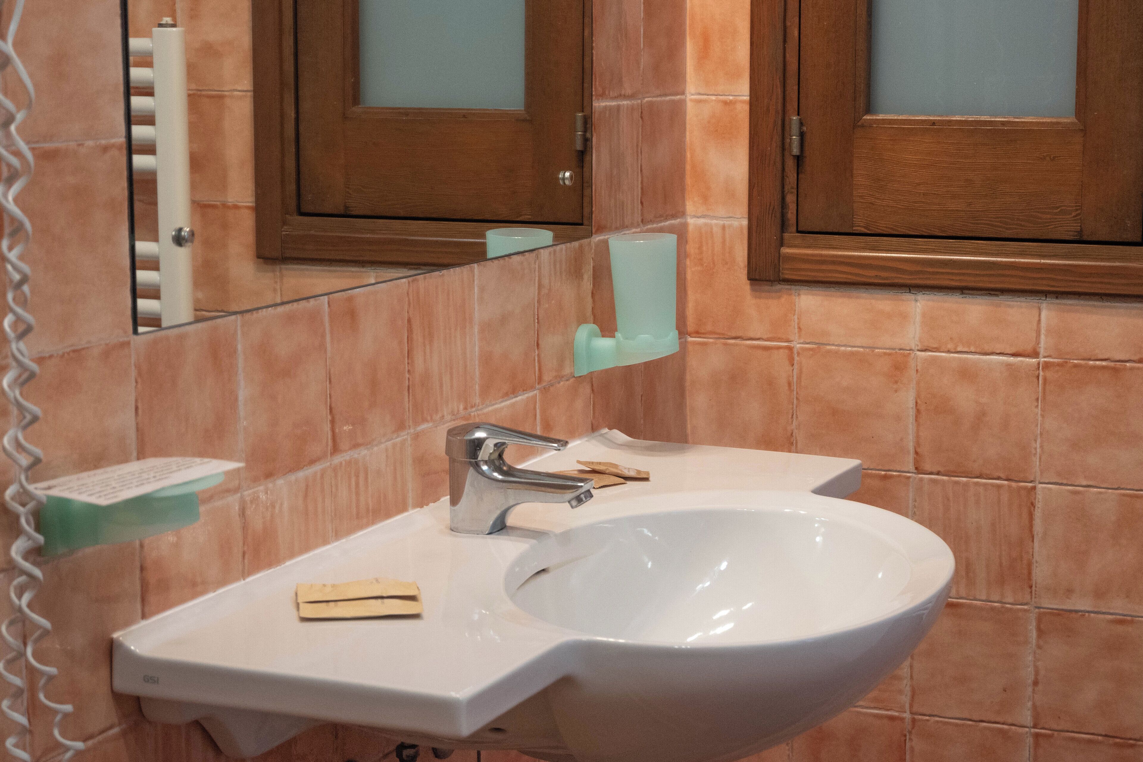 Un bagno con un lavandino bianco, uno specchio e una porta in legno.