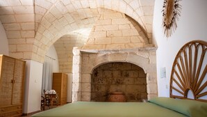 Ein Zimmer mit einer Decke aus Steinbögen, einem Bett mit einer grünen Bettdecke, einem Weidenkopfteil und einem Holzschrank.
