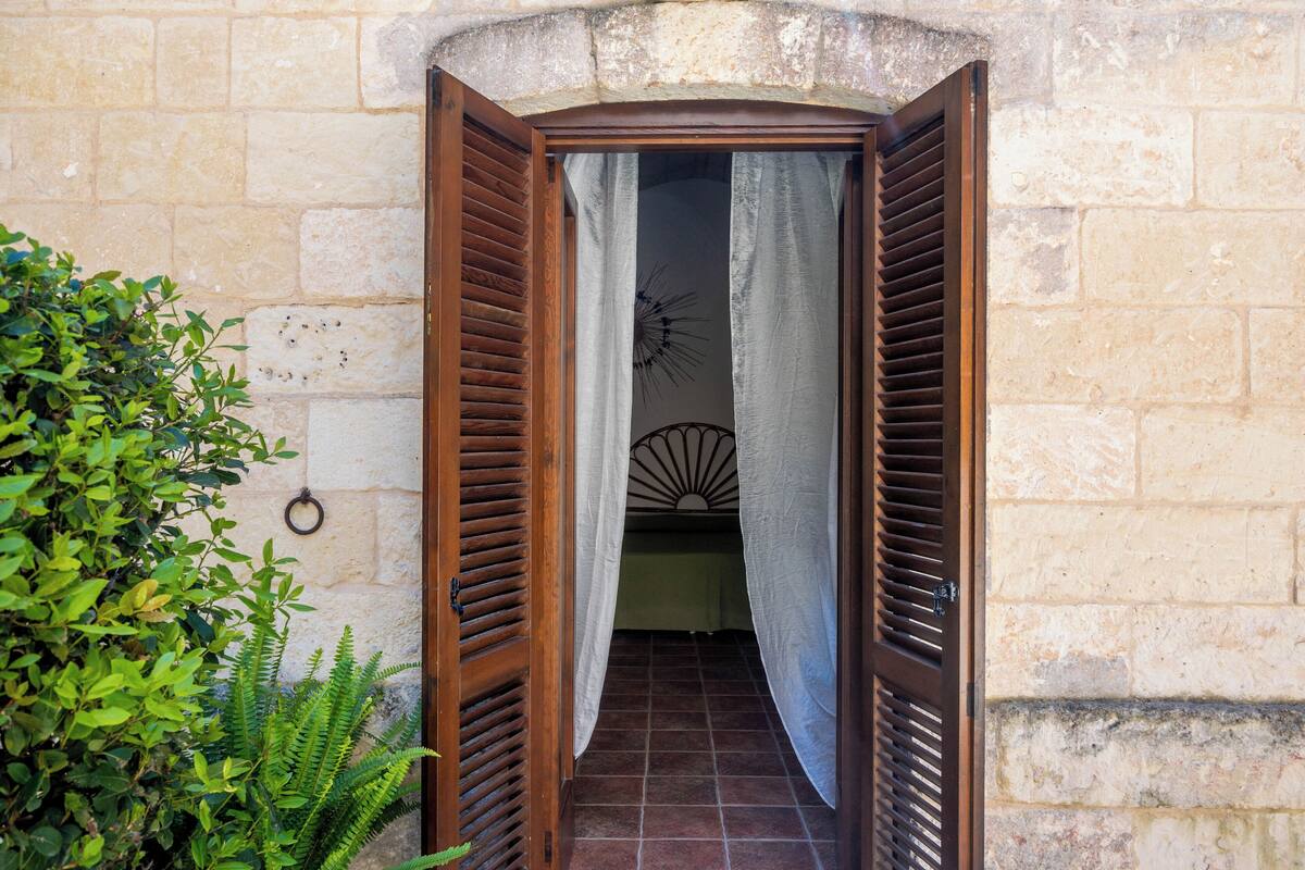 Puerta de madera abierta con cortina, que da a un cuarto con cama y un adorno en la pared.