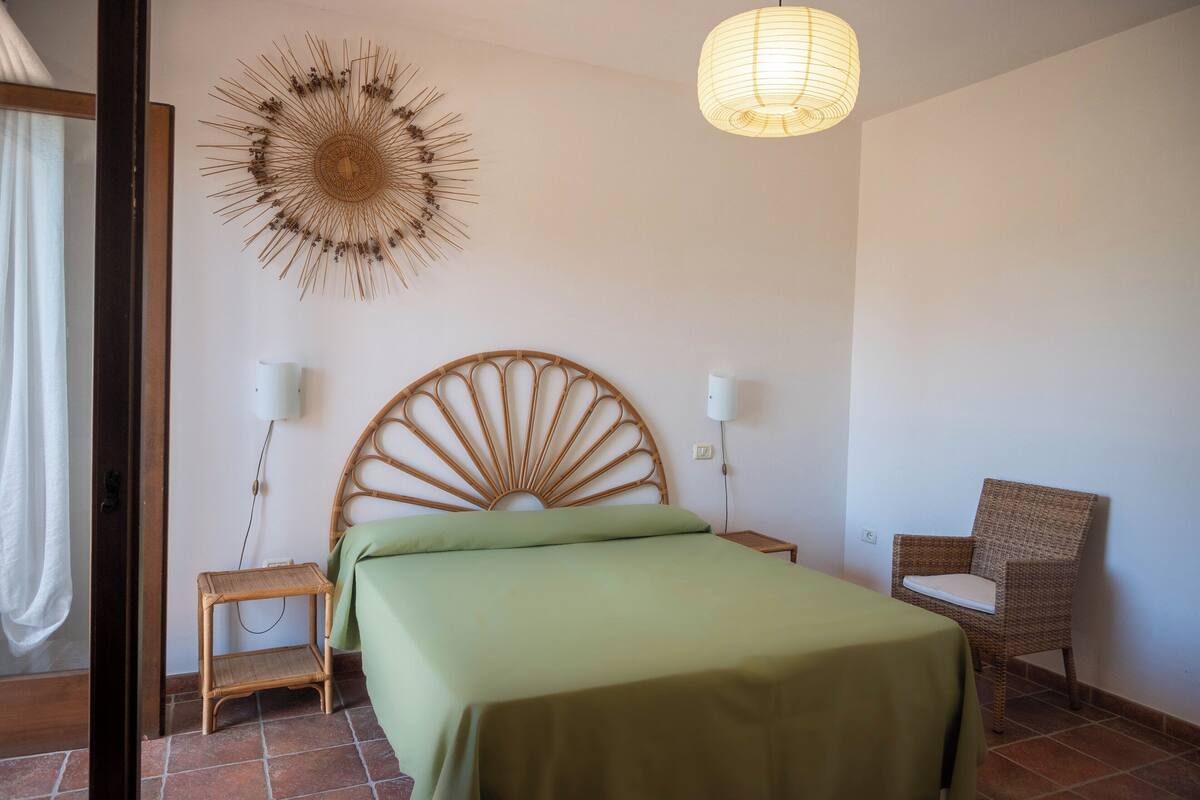 Un dormitorio con una cama, una silla, un adorno en la pared y una lámpara colgante.