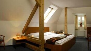 Un dormitorio con techo inclinado, estructura de cama de madera, mesita de noche con lámpara y ventana con cortinas.