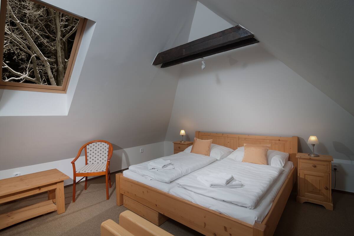 Un dormitorio con una cama de madera, una silla, una mesita de noche y un ventanal con vistas a árboles.