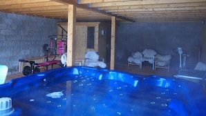 Un jacuzzi en una habitación de madera con paredes de piedra, equipo de ejercicio y sillones mullidos.