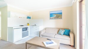 A compact living space with a kitchenette, a sofa, a coffee table, and a view of the sea. - Byron BaySide Central Studio Apartments (Byron Bay)