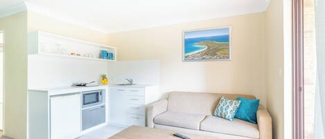 Un espacio habitable compacto con kitchenette, un sofá, una mesa de centro y vista al mar.