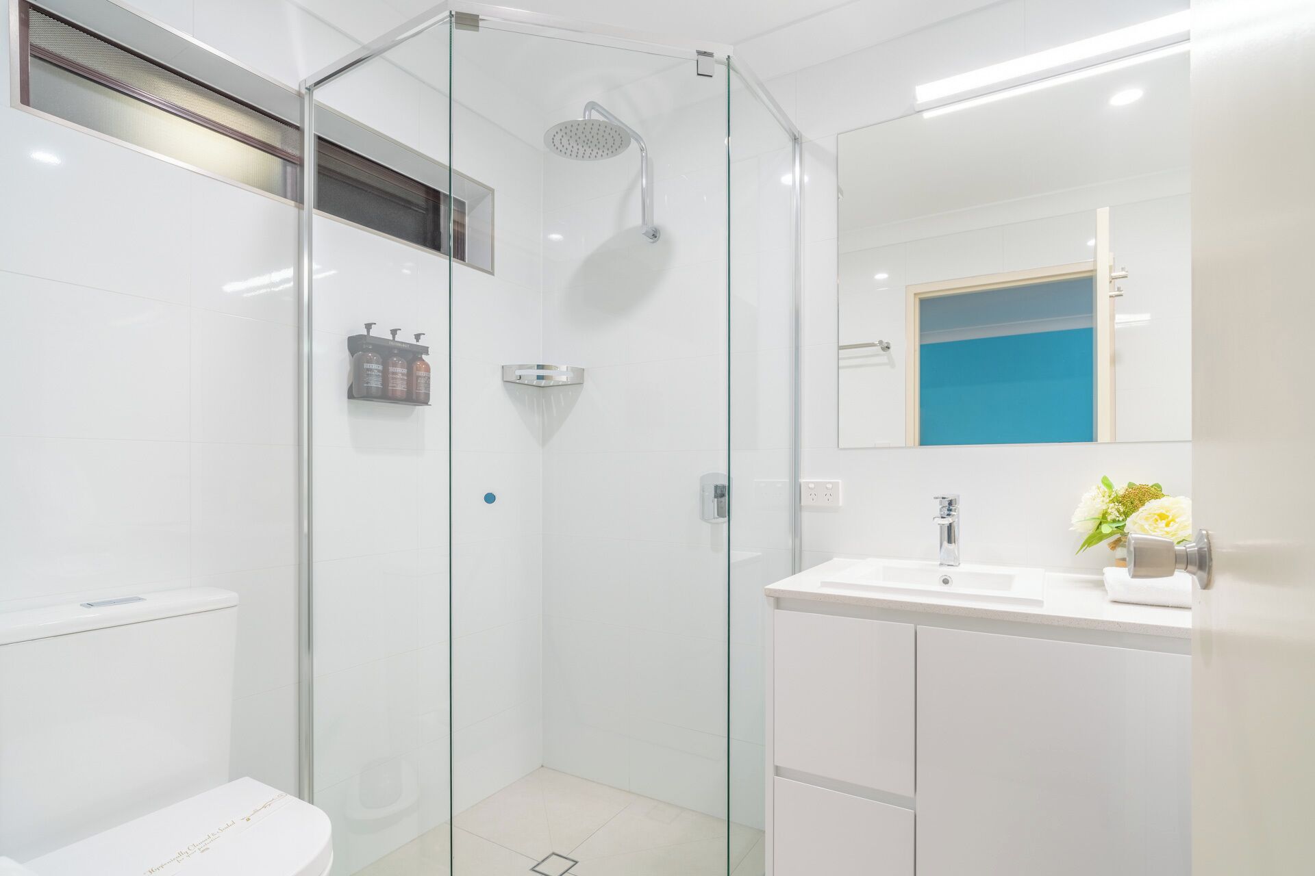 Un baño moderno con ducha de vidrio, lavamanos blanco y espejo.