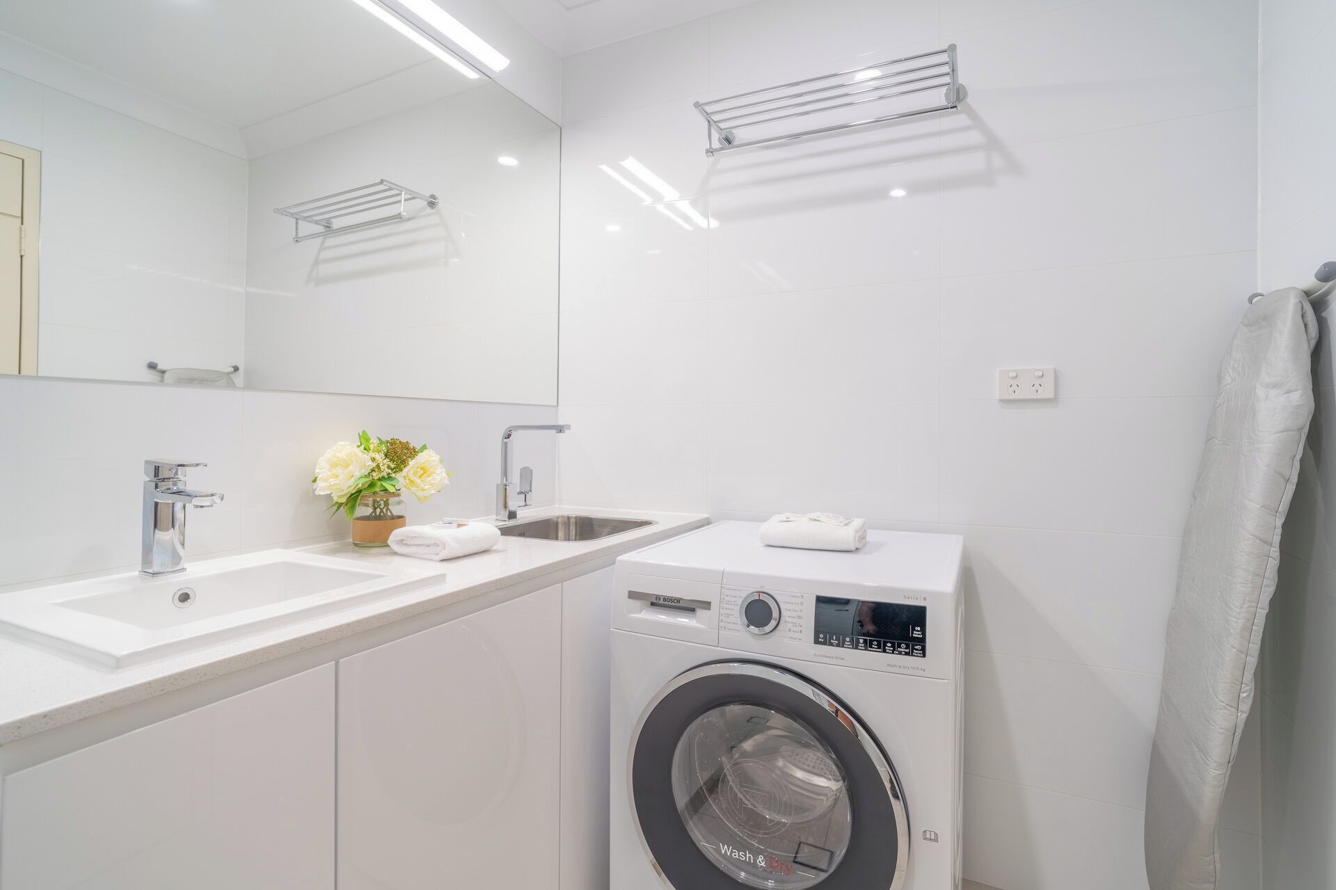 A modern bathroom with a washing machine, two sinks, and a towel rack.